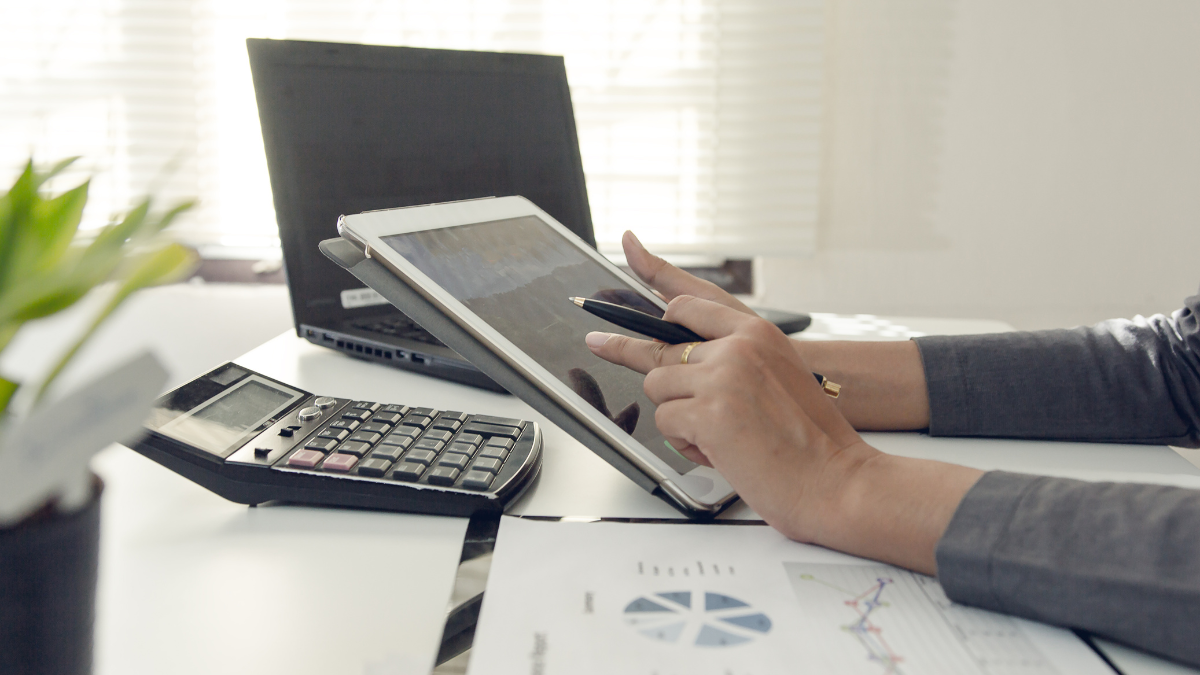 Business professional analyzing financial data on a tablet, with a calculator and compensation planning documents on the desk.